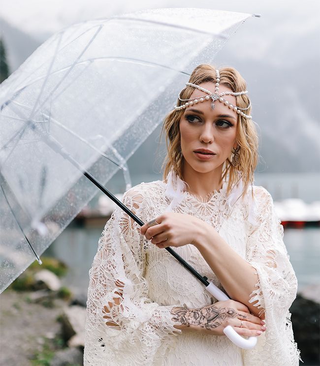 Une mariée en robe sous la pluie avec un parapluie.